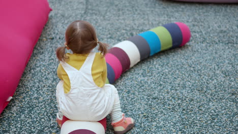 Una-Niña-Graciosa-De-3-Años-Finge-Montar-En-Una-Almohada-Larga-Y-Colorida-En-Una-Zona-De-Juegos-De-Un-Centro-Comercial