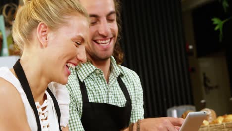 Smiling-waiter-and-waitress-standing-at-counter-using-digital