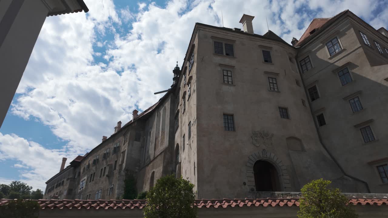 Exterior view of Český Krumlov Castle in Czechia, showcasing its historic architecture and stone facade under a partly cloudy sky