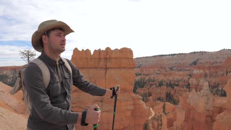 a hiker man in a cowboy hat looks around the canyon scenery.