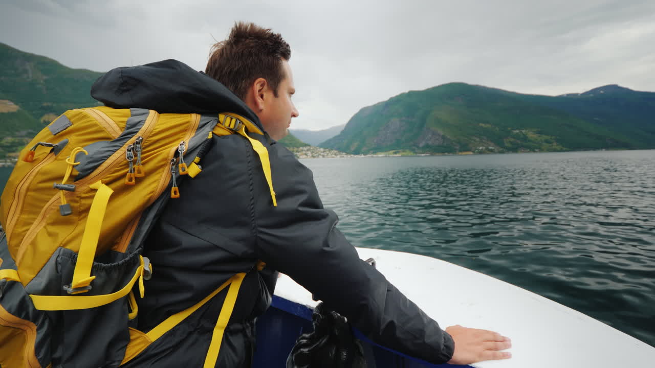 En mannlig reisende står på baugen av et lite cruiseskip som seiler på en pittoresk fjord i Norge. 4K-video.