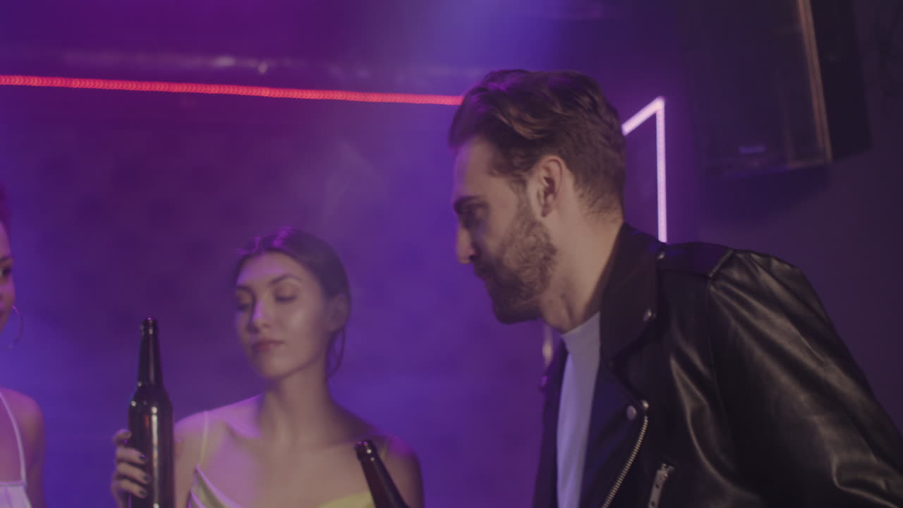 grupo de cuatro jóvenes amigos brindando con una botella de cerveza mientras bailan en la discoteca 1