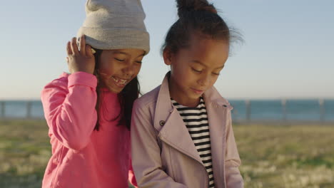 close up portrait of two little girls smiling happy playing games using smartphone mobile technology enjoying seaside park