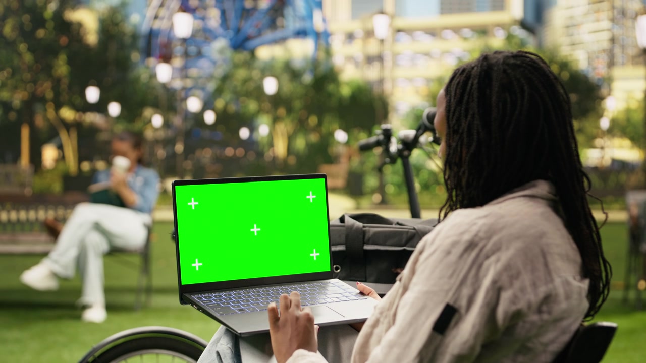 Schermo verde chroma key su laptop tenuto da un corriere in un parco urbano