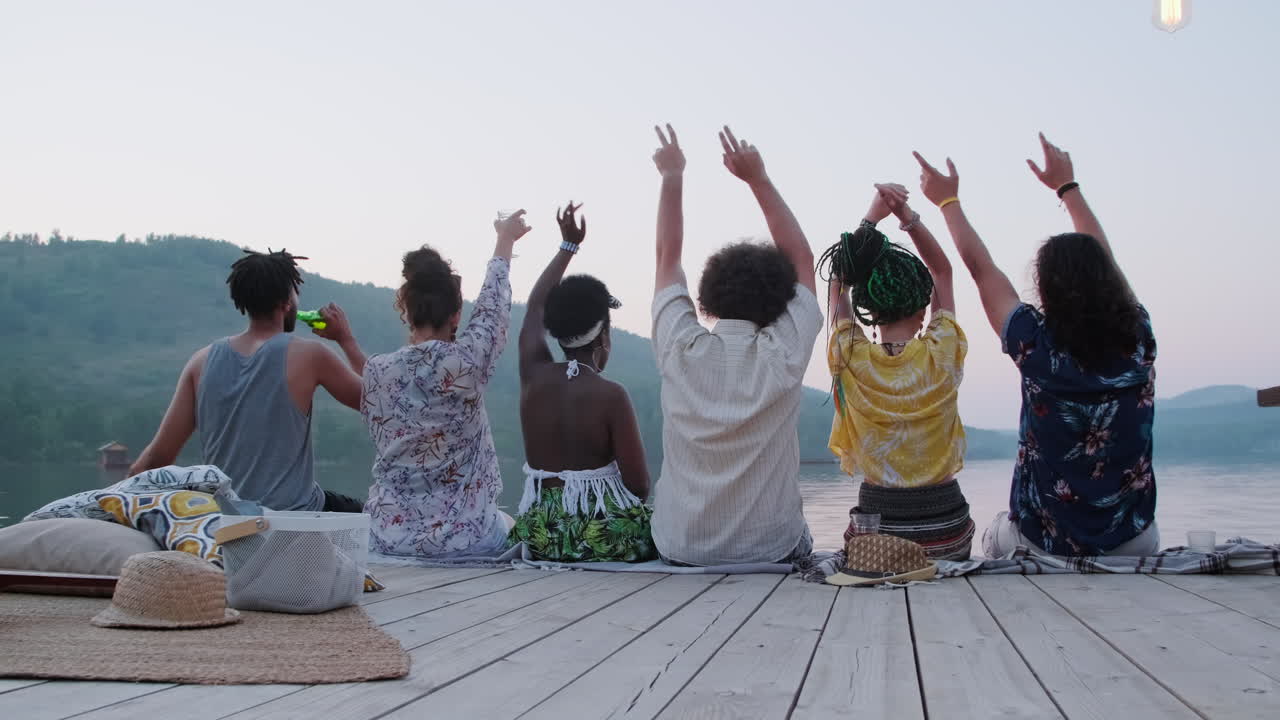 Friends Sitting on Pier and Waving Arms at Lake Party