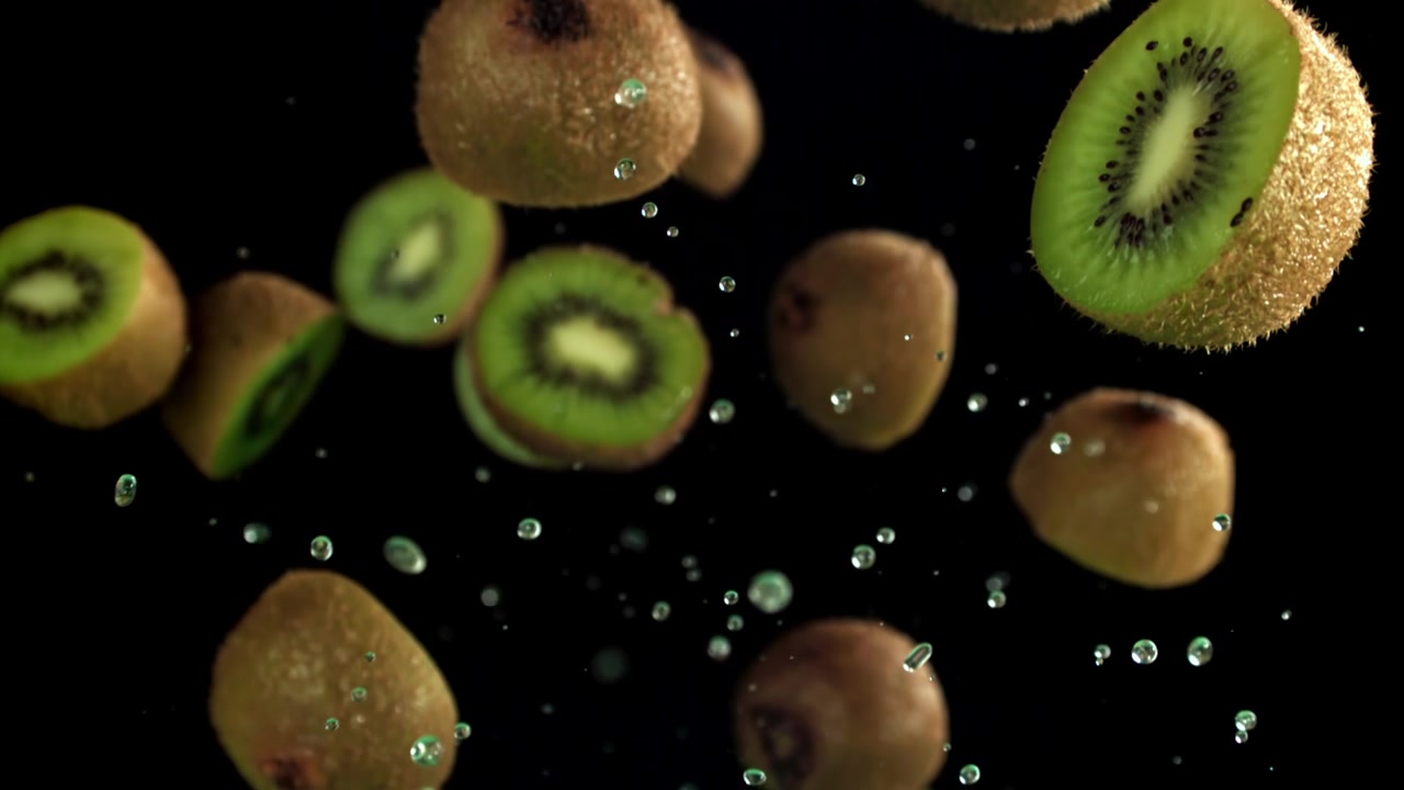 Mitades de kiwi fresco y kiwis enteros cayendo con salpicaduras de agua en cámara lenta