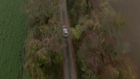 Single-white-car-driving-between-autumn-trees,-drone-top-down-tracking-or-following-view