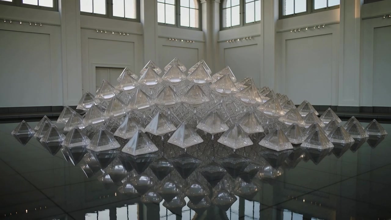 Activating motors, translucent pyramids rising into peaked wave on black pool at gallery