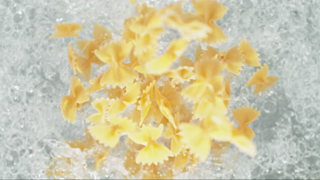 farfalle pasta cayendo en una olla de agua hirviendo haciendo un salto en cámara lenta, vista de la mesa