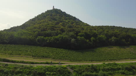 Couple-on-cycling-trip-below-Děvičky-castle-hill-in-Moravia,-drone