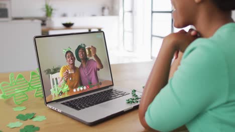 Smiling-african-american-male-friends-with-beer-wearing-clover-shape-items-on-video-call-on-laptop