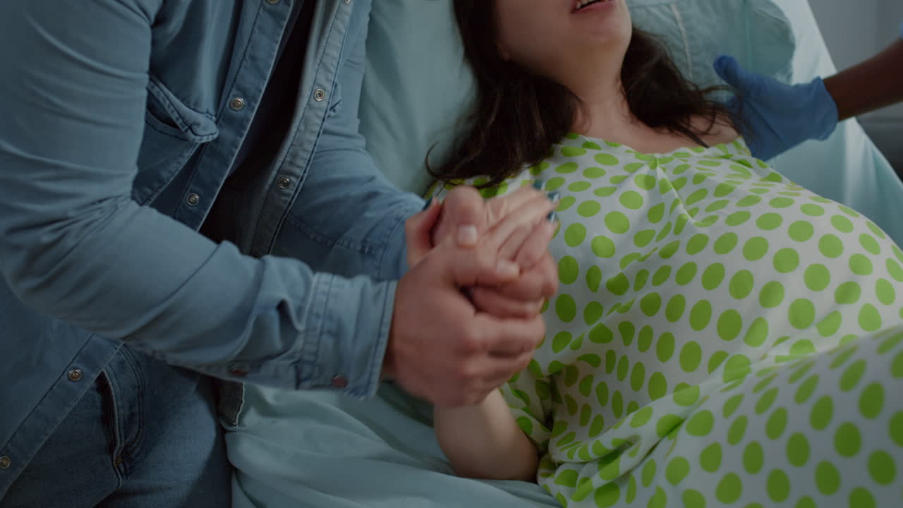 Woman in pain from childbirth holding hands with husband