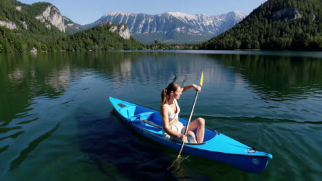 woman kayaking on a clear blue lake with mountains in the background