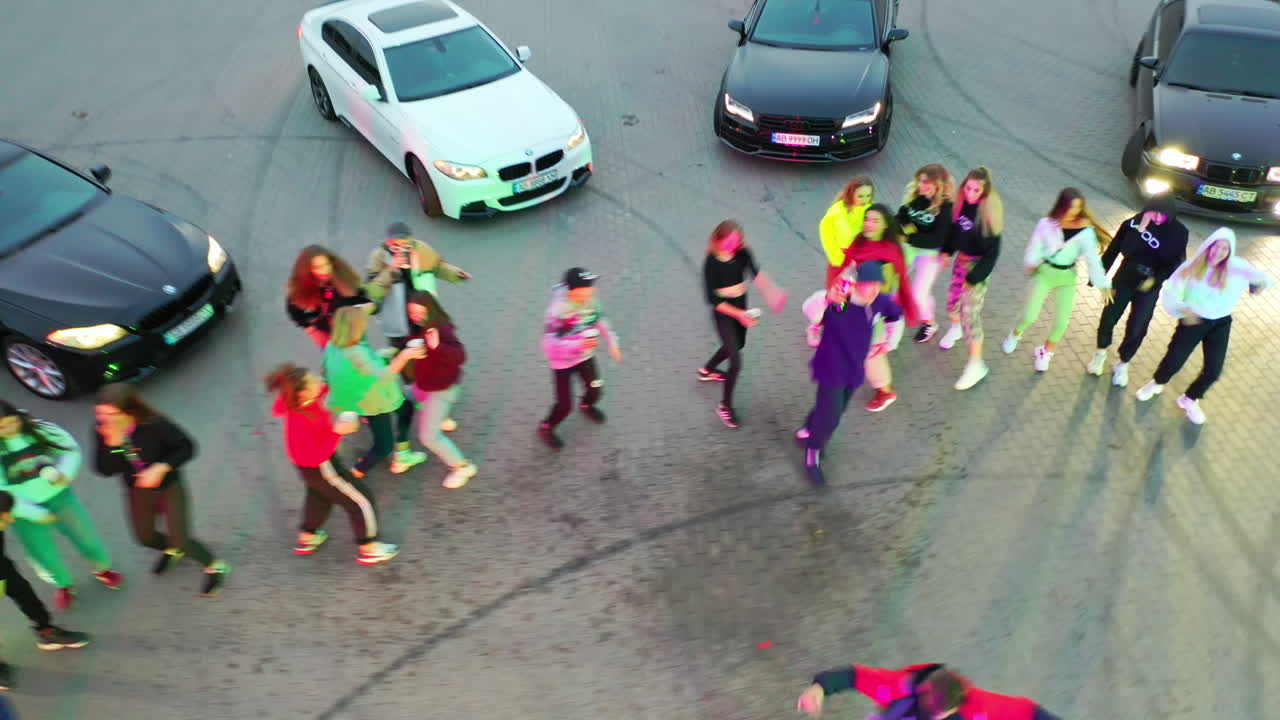 Young people having party outdoors at the drift field. Guy in cap pouring beverages into cups. Race cars stand beside.