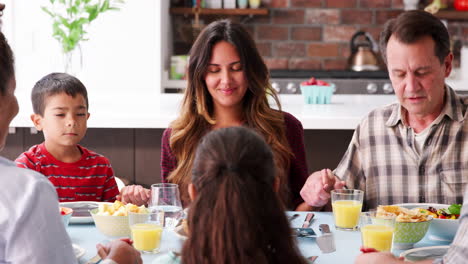 Familia-Multigeneracional-Orando-Antes-De-Comer-Alrededor-De-La-Mesa-En-Casa