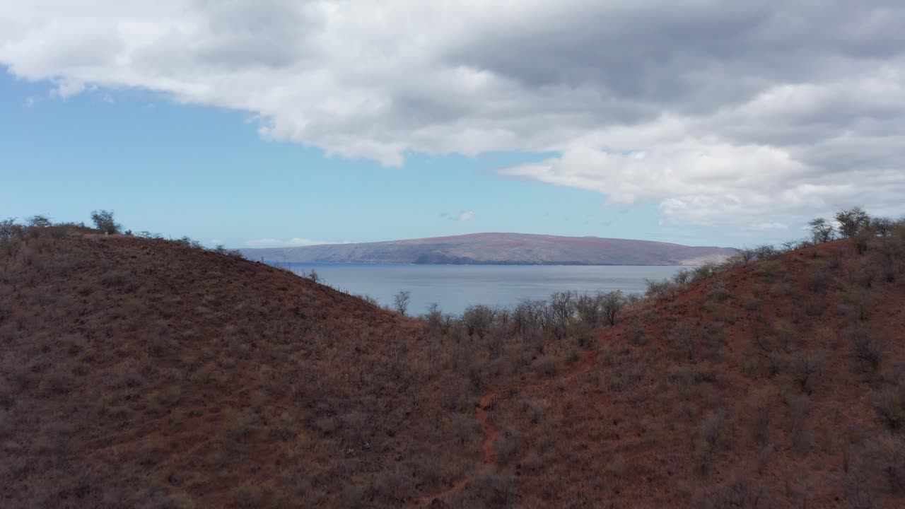 Aerial shot flying over the top of a cinder cone crater to reveal the sacred island of Kaho'olawe off the coast of Maui in Hawai'i