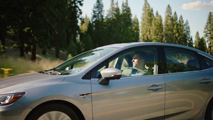 Enregistrement d’une berline argentée dont le conducteur roule à la même allure sur une route bordée de pins, portant un sweat à capuche et une ceinture de sécurité