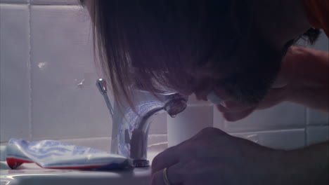 man soaks toothbrush under tap before brushing teeth over sink, close up shot