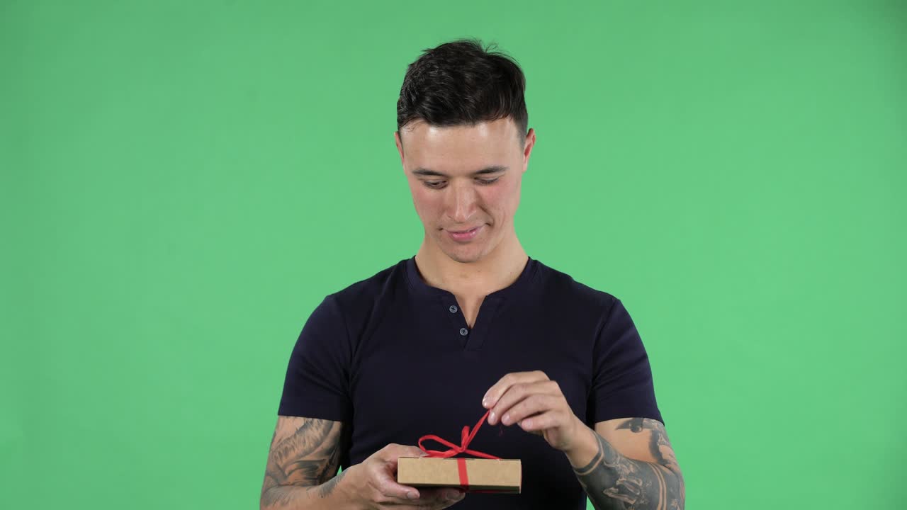 잘생긴 젊은 남자의 초상화가 카메라를 바라보고 와우 놀라움과 기으로 선물을 열고 있습니다.