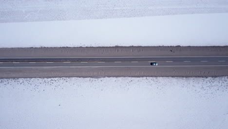 Car-drives-by-white-salt-flats-in-Jujuy-in-Argentina,-overhead-aerial