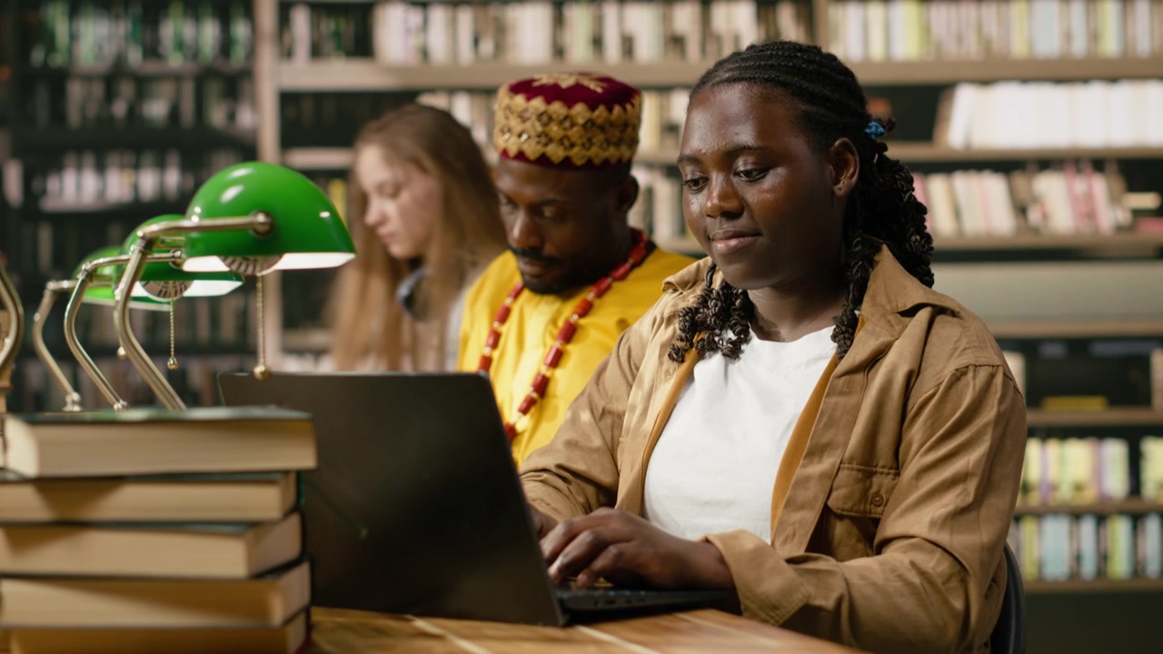 Woman learner studying on laptop and typing beside stacks of books