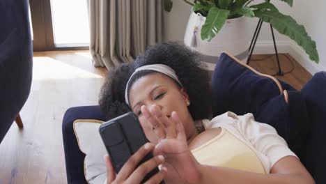 african american plus size woman lying on sofa and using smartphone, unaltered, in slow motion