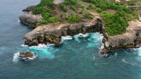 turquoise blue tropical water crashing onto the cliffs at nusa ceningan island in indonesia, aerial