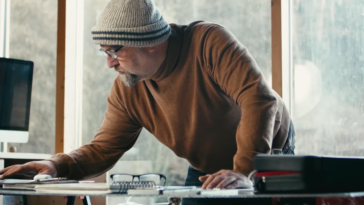 An older hipster designer works on a project in his glass-walled office