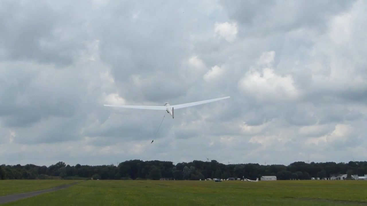Spilstart af et hvidt svævefly over en hvid flade ind i den skyede himmel.