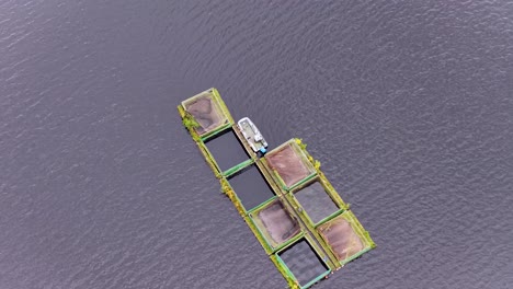 overhead drone footage shows a boat moored to floating fish cages on calm reservoir water, with steady camera movement and soft natural daylight