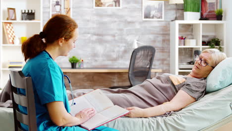 revealing shot of an old lady lying in hospital bed while a nurse is reading a book to her