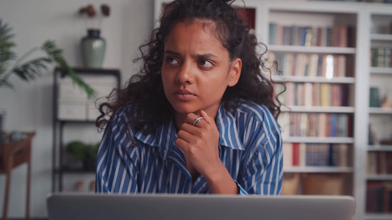 Indian ethnic woman sit at home office desk with laptop thinking of inspiration