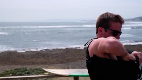 young man getting ready to surf in the cold water of chile punta de lobos pichilemu while putting on his wetsuit