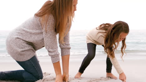 mother and daughter drawing in the sand