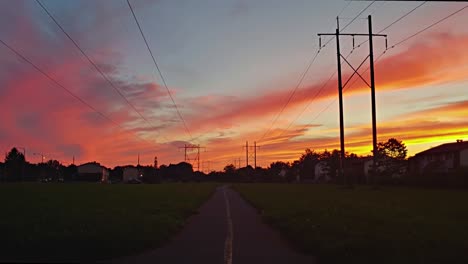 timelapse of a trail on a summer evening with a huge sunset and lights turning on as it gets dark while cars drive by in the distance