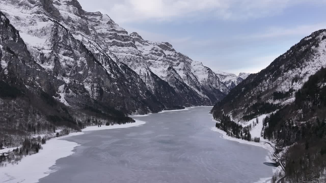 Henkeäsalpaava näkymä Klöntalersee-järvelle Glarusissa, Sveitsissä, lumihuippuisten vuorten kohotessa jäätyneen järven yllä, luoden tyynen ja majesteettisen talvimaiseman.