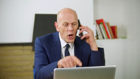 an angry mature businessman is talking on the phone in his home office