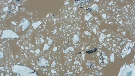 Antena-De-Arriba-Hacia-Abajo---Agua-Marrón-Con-Trozos-De-Hielo-Flotante-En-El-Lago-Glacial