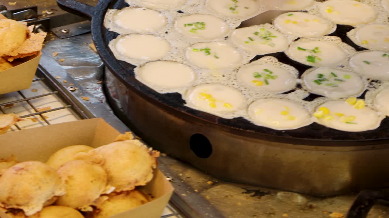 Vendor prepares and serves Thai coconut pancakes on hot griddle at bustling outdoor market