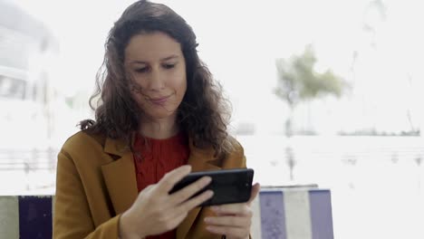 chica enfocada sentada en un banco y usando un teléfono inteligente
