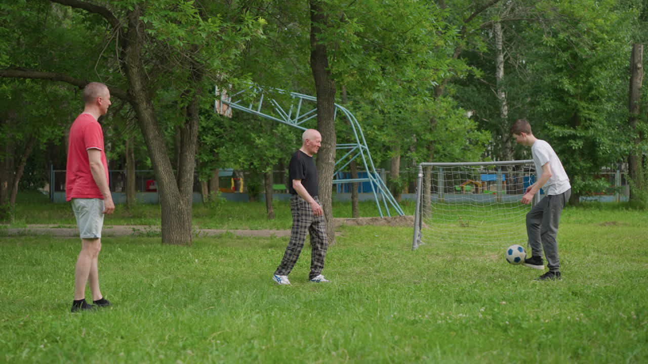 Grandfather, father, and son share a bonding moment as they play football together, the grandfather passes the ball to his grandson, who kicks it towards his father
