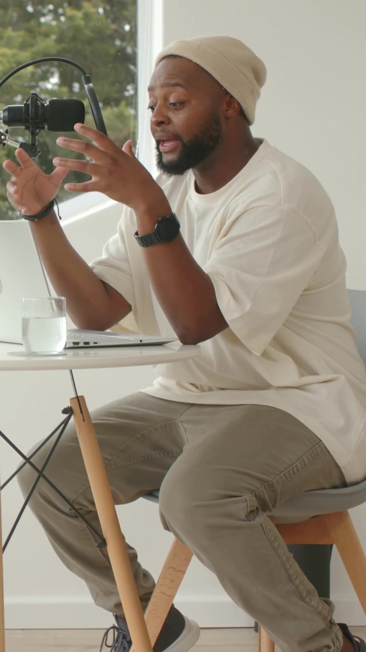 After quiet pause, podcaster leaning toward laptop and mic, speaking and gesturing to explain ideas