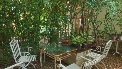 garden furniture with white chairs and a glass table under green trees in a summer backyard