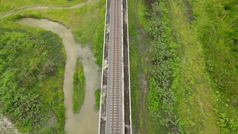 an aerial footage revealing a railway, birds flying, grassland on the right, a canal of water on the left, saraburi, thailand