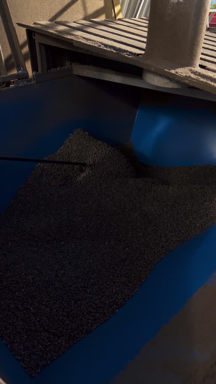 Worker mixes grains in a bin. Industrial equipment for agribusiness. Industry for compound feed. Feed mill. Close-up. Vertical video