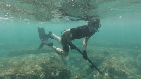 front facing shot of spearfisher snorkeling in shallow crystal clear waters in the mediterranean sea while waves crush at shore