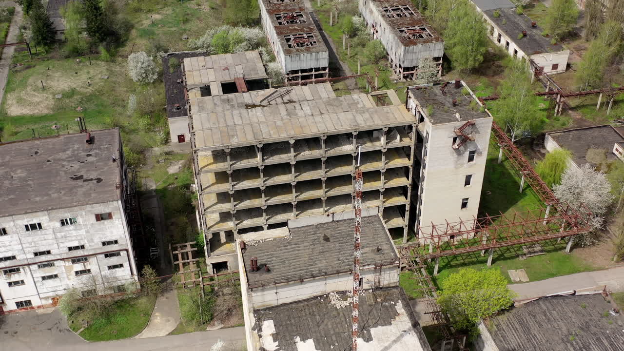 Old industrial edifices. Ancient manufactory with ruined buildings in abandoned zone in springtime. Camera rising up.