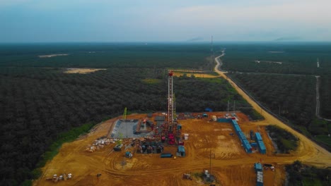 Cinematic-Drone-Footage-of-Onshore-Drilling-Rig-equipment-structure-for-oil-exploration-and-exploitation-in-the-middle-of-jungle-surrounded-by-palm-oil-trees-during-sunset-and-high-oil-price