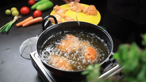 turning upside-down the fried chicken pieces with a fork while frying in a deep pan