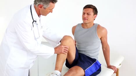 Mature-doctor-checking-sportsmans-injured-knee